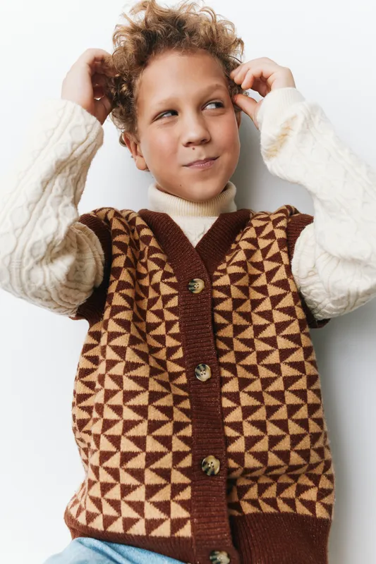 Authentic moment of school lifestyle with a curious child wearing a geometric brown vest over a knit sweater, capturing a playful, unposed game vibe.