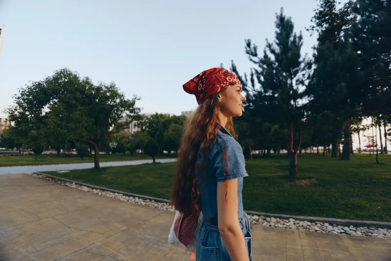 lifestyle woman in modern boho-western denim street style walking outdoors, film color effect enhances natural light and casual vibe in park setting