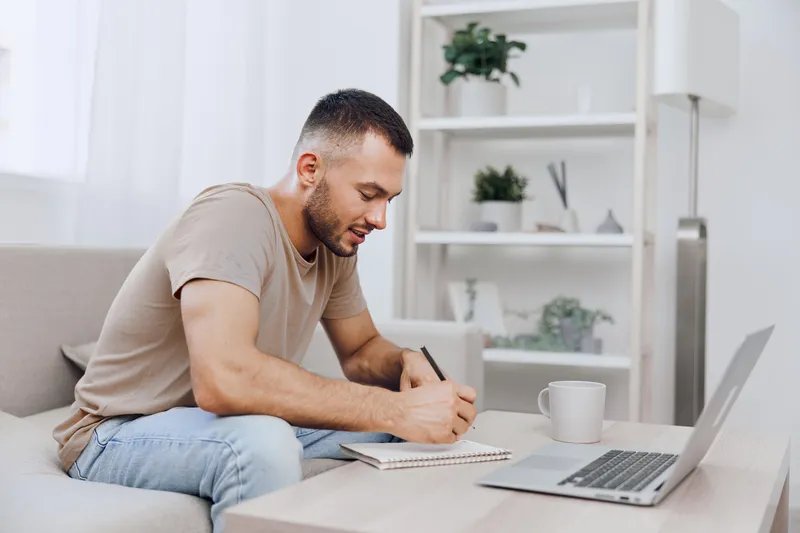Thoughtful man working on a creative project while sitting on a cozy sofa, surrounded by natural light and a minimalistic interior design.