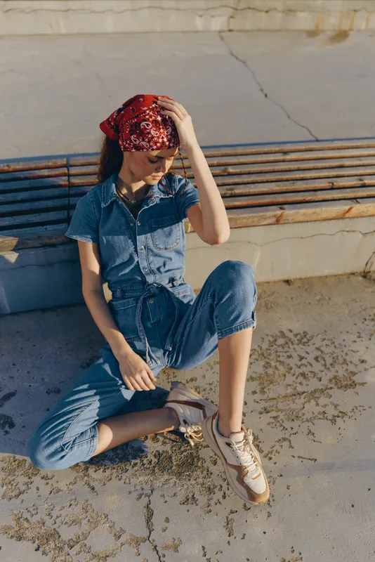 Lifestyle woman in modern boho-western denim street style with a red bandana, relaxed pose, and natural sunlight in film color tones outdoors.