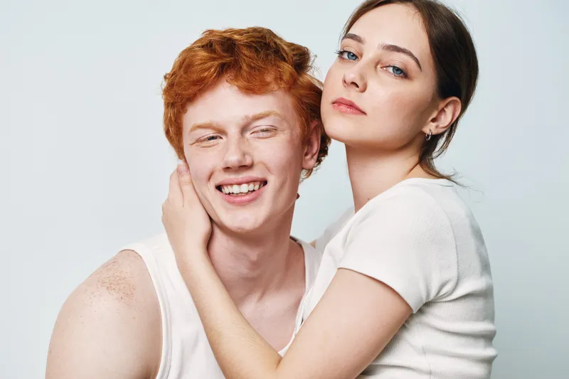 Young couple with red hair and fair skin posing close together in white casual clothing on plain light background for friendship and relationship concept.