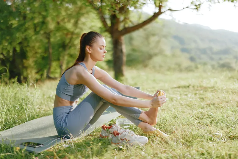 Young woman in sportswear practicing yoga outdoors, demonstrating relaxation and mindfulness in a serene green setting with vibrant colors