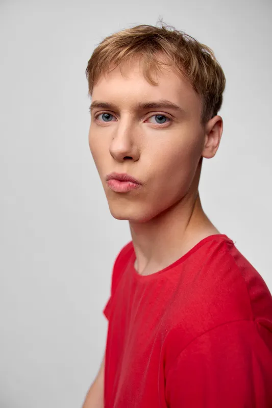 Young man in a red shirt in a studio headshot with balanced lighting and a neutral background, presenting a modern calm fashion vibe for marketing and editorial use