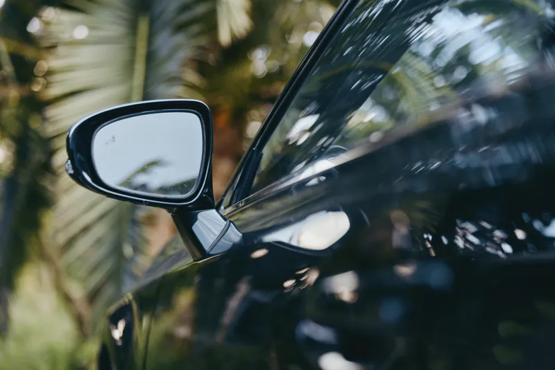 Car side mirror reflection with palm tree on glossy black car window, closeup shot of modern vehicle exterior showing shiny paint, mirror detail and outdoor tropical mood