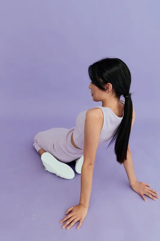 young woman in activewear stretching on purple floor, fitness, flexibility, casual workout, long black hair, white sneakers, studio background
