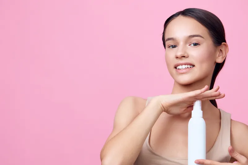 Young woman showcasing a skincare product against a pink background, expressing confidence and elegance with natural beauty