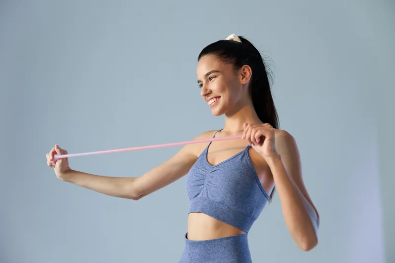 Active woman sport fitness stretching with resistance band, wearing blue workout clothes, smiling and focused during indoor exercise session.