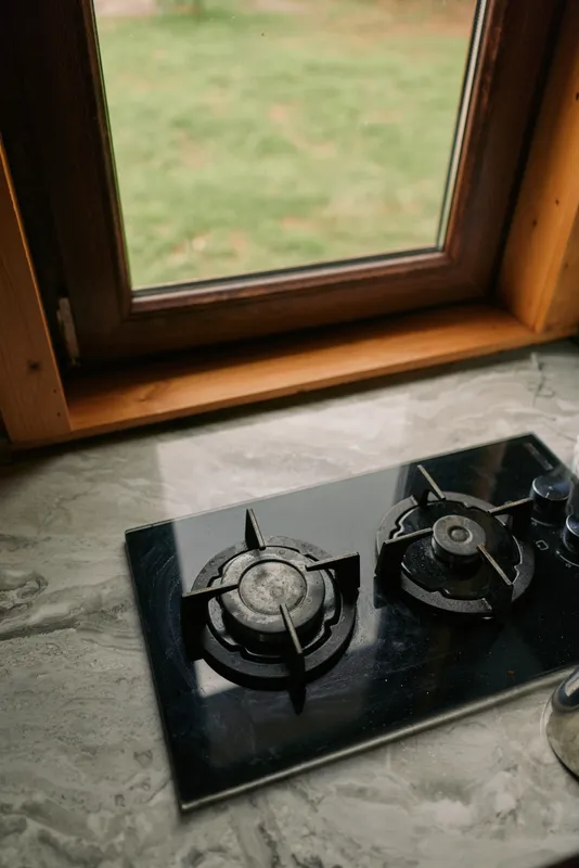 Gas stove with two burners on a marble countertop beside a wooden window frame, capturing a simple kitchen scene with natural light, a calm domestic cooking mood, and quiet home ambience.
