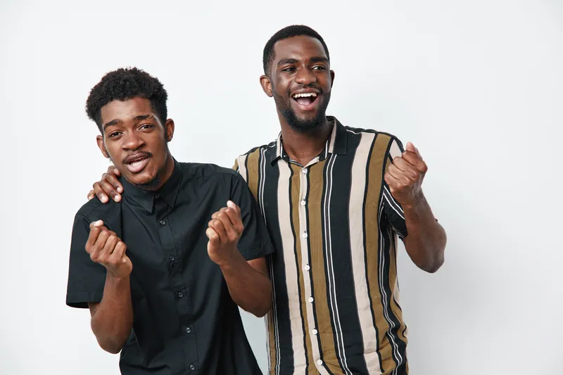 Two young African American men with dark skin smiling and celebrating together in casual clothing on white background. Friends, happiness, joy and positive emotions.