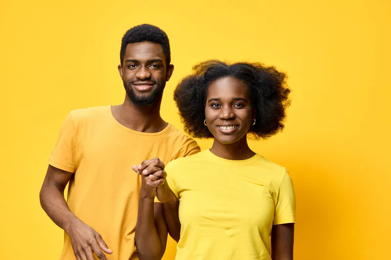 Happy young African couple in matching yellow outfits smiling together against a bright yellow background, symbolizing joy, love, and togetherness