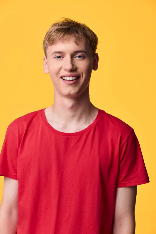 Young man in a red shirt smiles against a yellow background, casual fashion vibe with bright studio lighting, warm energy and a youthful lifestyle for approachable everyday style visuals