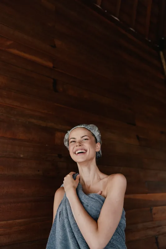 smiling woman wrapped in towel enjoying spa moment with joyful expression, wooden background and natural light creating warm atmosphere