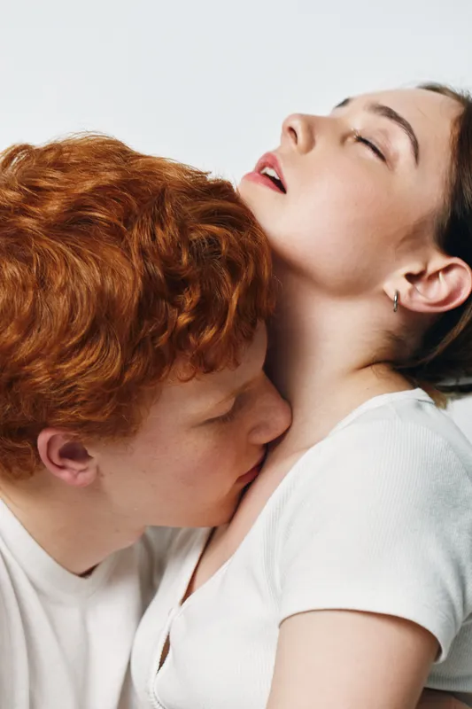 Couple, intimacy and affection with man kissing woman neck in white clothes for romance, connection and love closeup. Relationship, passion and tenderness with eyes closed on light background.