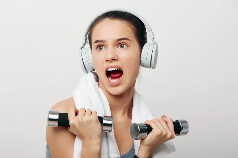 Woman fitness in studio, sport themed workout with dumbbells, headphones and towel wrapped around her neck, displaying focus, effort and healthy training in action.