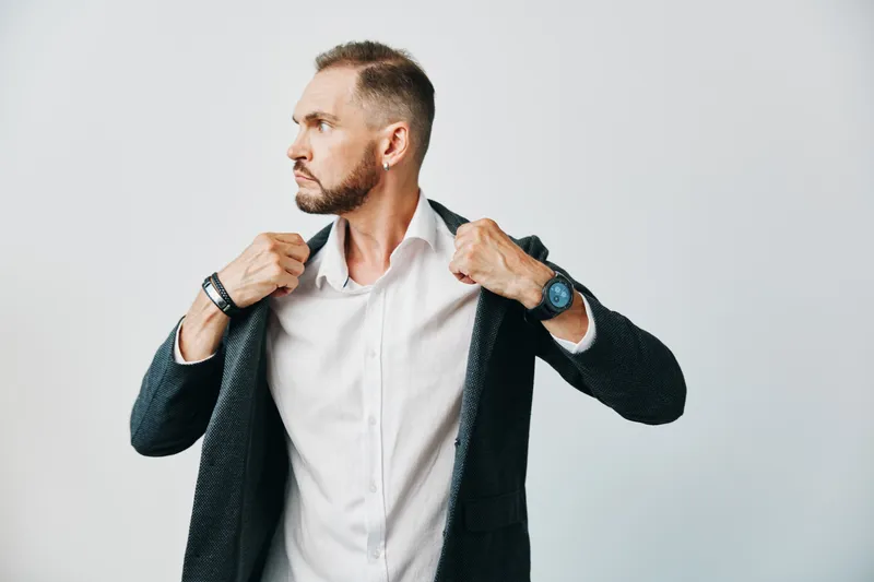 A sharp business professional man stands against an isolated light background, confidently adjusting his suit jacket while glancing aside, exuding focus, control, and readiness for a task.