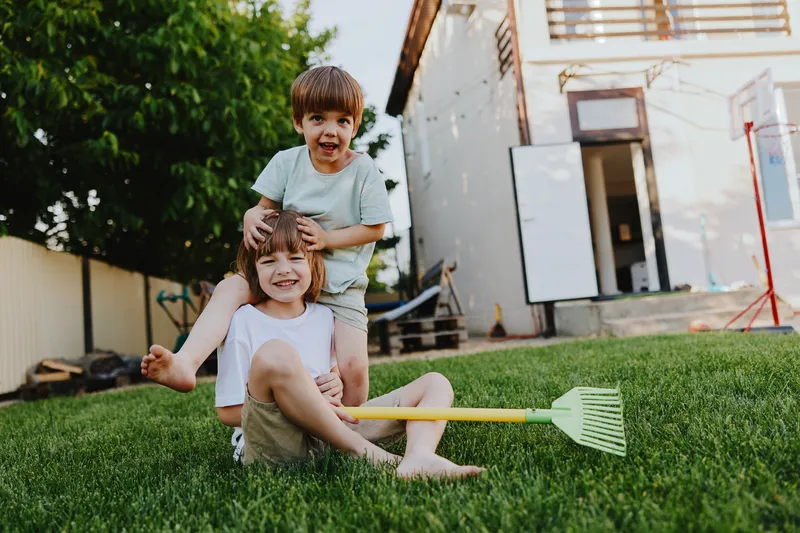 Two joyful boys playing outside in the sunny garden, expressing happiness and laughter while enjoying a carefree summer day.