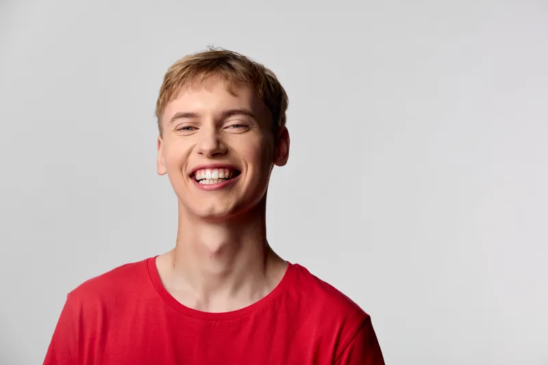 Smile, man in a red shirt, bright studio scene captures happiness and confidence, clean background, friendly vibe suitable for lifestyle, positivity and promotional content