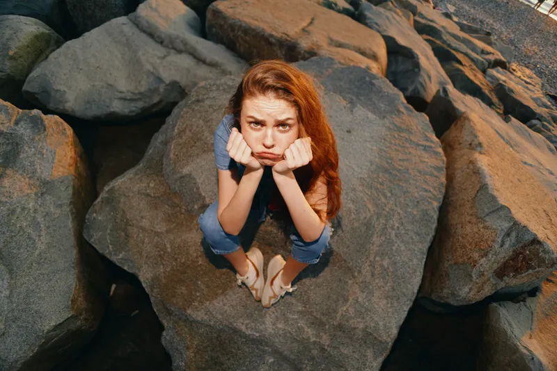 frustrated woman sitting on rock in modern boho-western denim street style with film color tones under natural sunlight outdoors