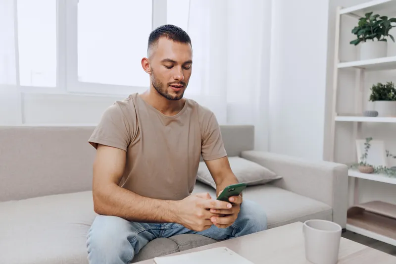 Engaged man using smartphone in a modern home setting, displaying casual style and a relaxed atmosphere, perfect for lifestyle and technology themes.