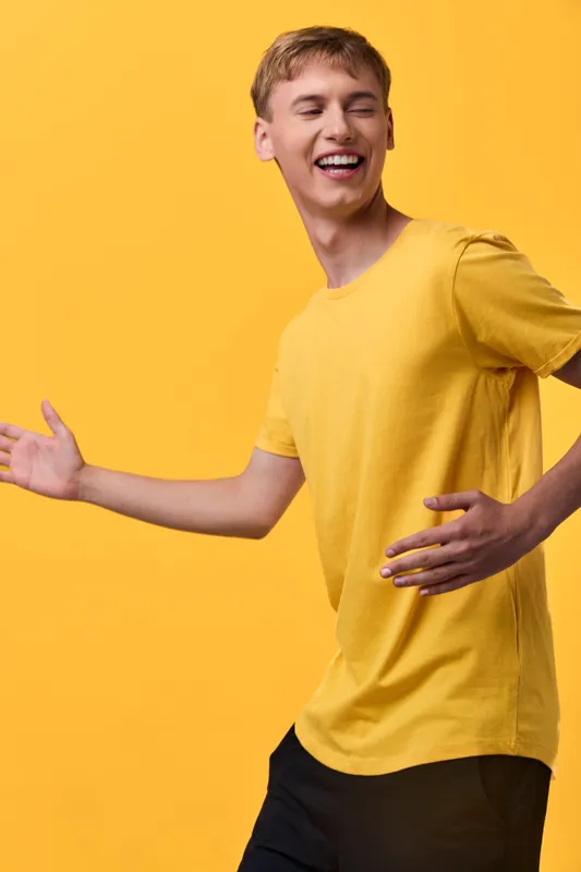 Joyful man in a bright yellow shirt moves with a wide smile and open arms, capturing dynamic energy against a solid yellow backdrop. Perfect for lifestyle, fashion, or happiness themes, branding.