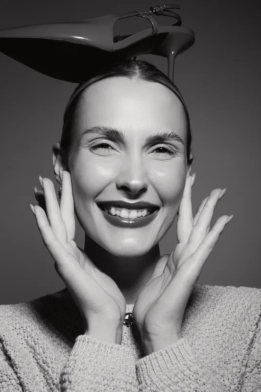 Happy Caucasian woman with light skin smiles joyfully, hands framing her face. Black and white portrait with soft lighting, concept of beauty, happiness, and positive emotions.