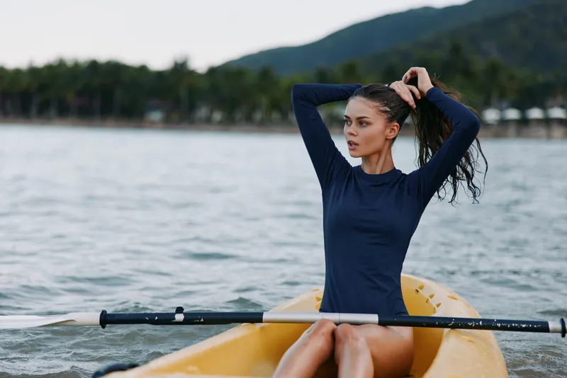 woman kayaking on lake wearing long sleeve shirt, holding paddle, outdoor adventure, summer activity, nature, water sport