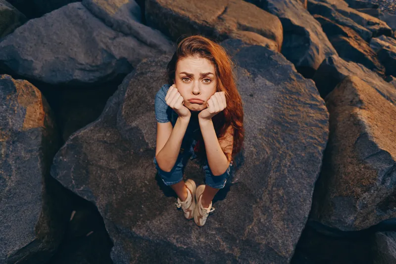 Lifestyle woman in modern boho-western denim street style, sitting thoughtfully on rocks, captured with film color for a natural, warm tone and relaxed mood.