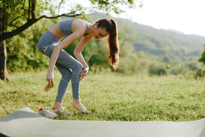 Young woman practicing yoga outdoors in a green park, wearing a blue athletic outfit, expressing focus and tranquility amidst nature