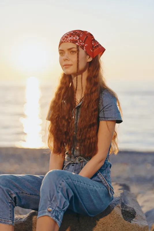 Lifestyle woman in modern boho-western denim street style sitting by the water at sunset with film color tones and relaxed natural mood.