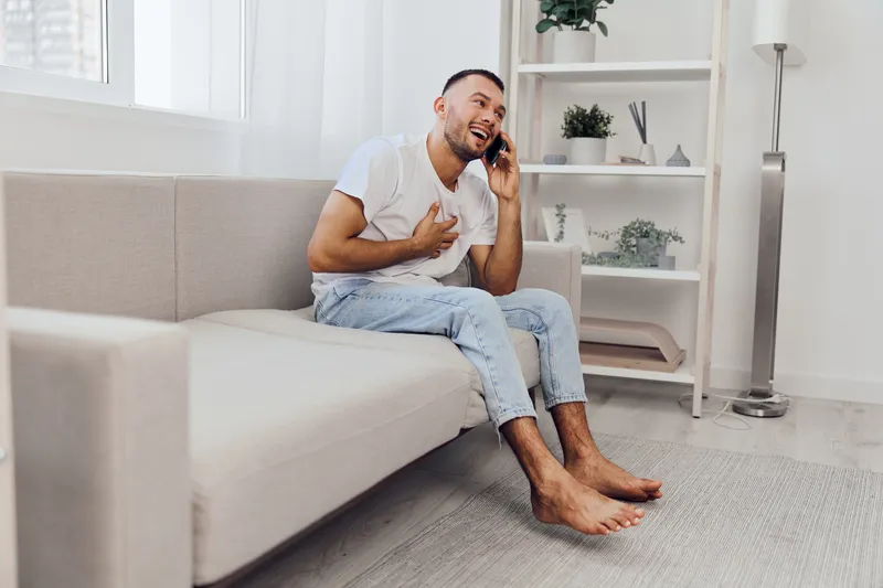 Happy man talking on the phone, embracing vulnerability and emotional connection while sitting comfortably in a cozy living space.