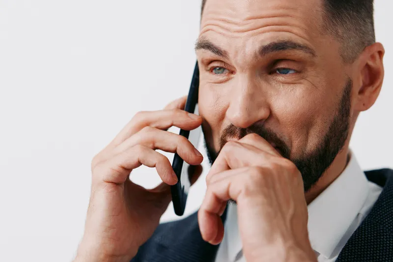 A professional man in business attire speaks on a mobile phone, showing thoughtful concern and confident focus against an isolated colored backdrop.