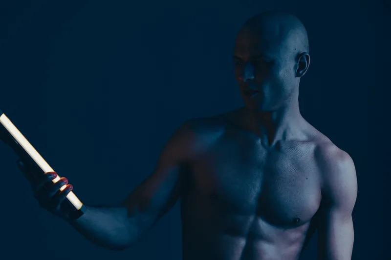 Engaging man showcasing fitness and strength under dramatic light, emphasizing muscular physique with a captivating, artistic flair in a blue and black color scheme.
