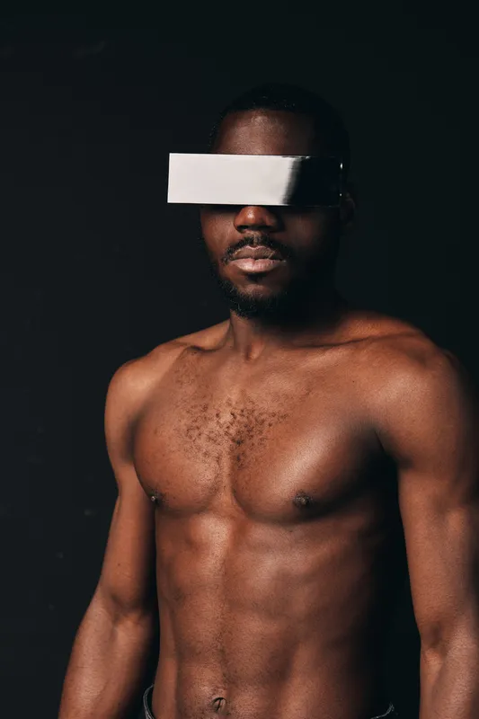 Creative conceptual portrait of African man with dark skin and muscular body wearing white blindfold against black background in visual artistic style for modern photography.