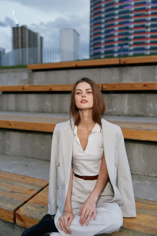 Confident businesswoman seated outdoors in professional attire, expressing determination and empowerment in an urban setting with modern architecture.