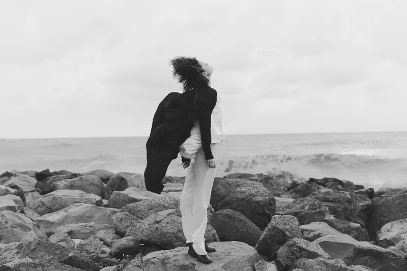 woman wind rocky shore sea solitude fashion monochrome outdoor dramatic landscape coast waves horizon mood contrast aesthetic seashore