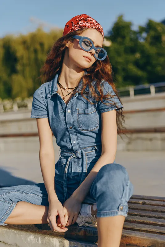 lifestyle woman in modern boho-western denim street style with blue sunglasses and red bandana, captured in warm sunlight with film color effect for a casual vibe