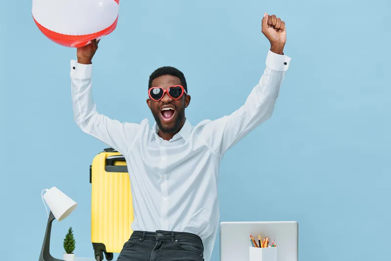Joyful man celebrating summer vacation at home, holding beach ball and wearing sunglasses, with bright yellow suitcase and cheerful expression. People lifestyle concept, relaxation, travel preparation