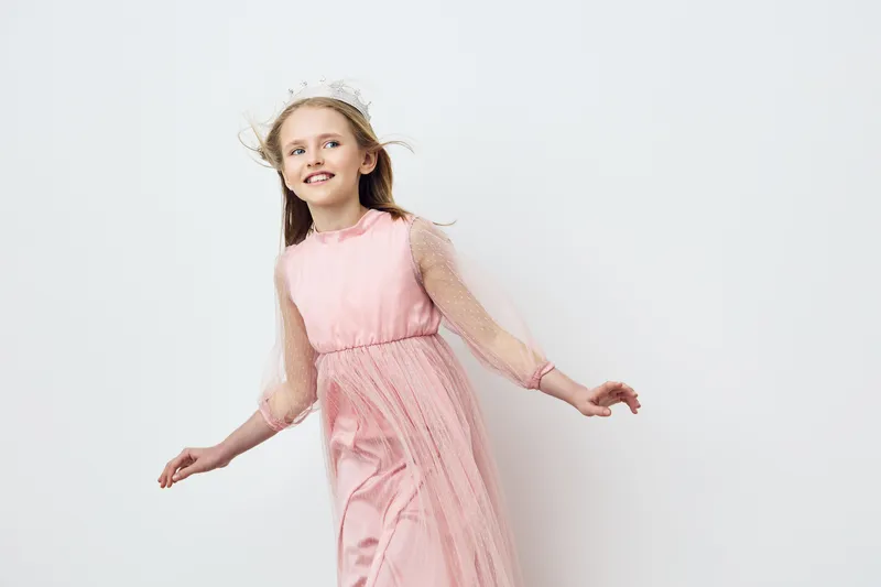 Joyful girl in a pink dress with tulle sleeves, smiling and posing playfully against a light background, perfect for spring or summer themes