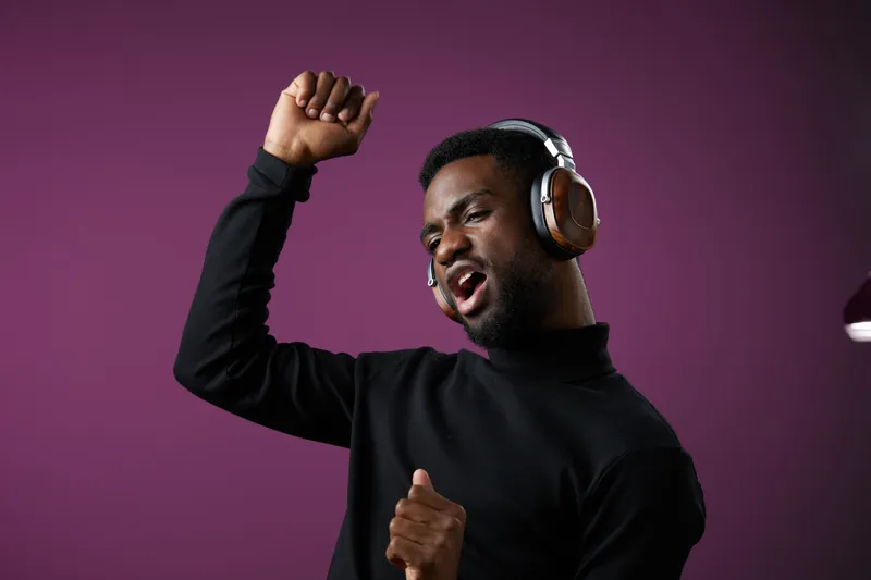 Happy young African man enjoying music with headphones, dancing joyfully against a vibrant purple background, embodying celebration and happiness