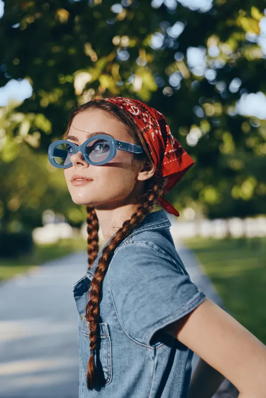 lifestyle woman in modern boho-western denim street style with blue sunglasses and red bandana in natural outdoor setting, film color effect