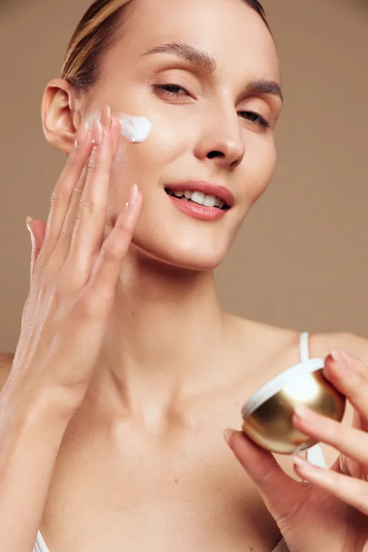 A woman performs a skincare routine, applying moisturizer with a gentle touch in a close up, warm lighting, revealing glowing skin and calm focus.