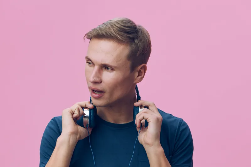 Portrait of thoughtful caucasian man wearing headphones dark blue sweater pose on pink background digital detox concept calm concentration