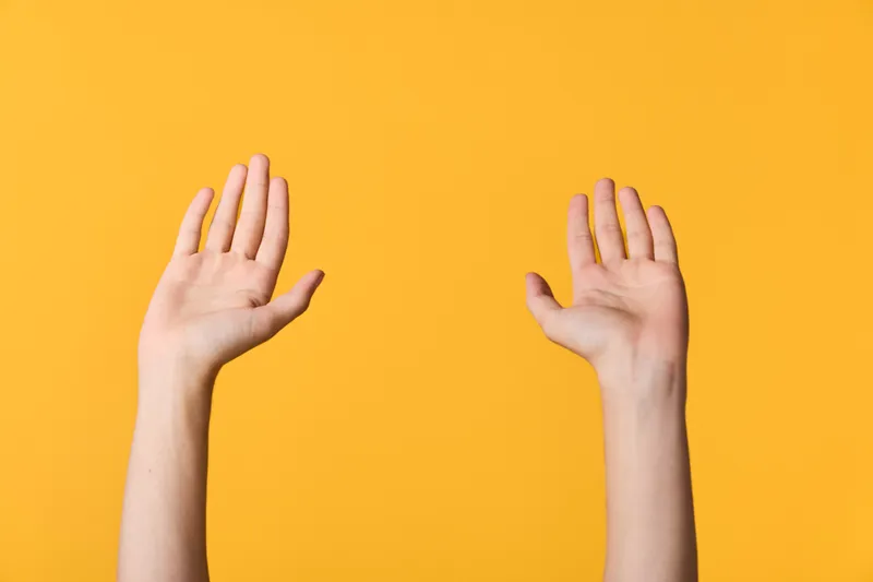 Hands raised against a bright yellow background, capturing a simple gesture of attention and openness. Minimalist concept suitable for communication, collaboration, safety, energy, or celebration in
