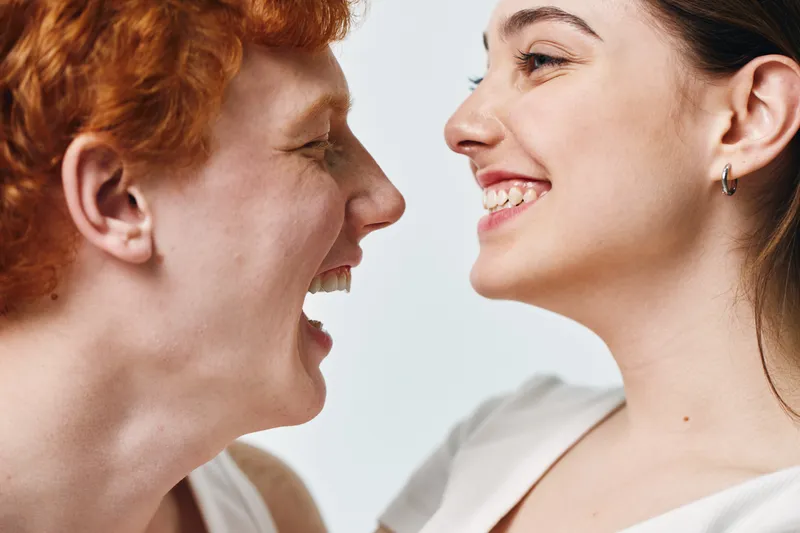 Friends, women and closeup smiling together with happy expressions and face to face interaction in casual clothing on white background studio shot.