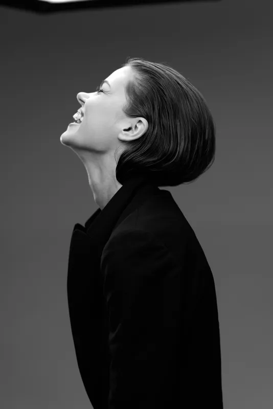 Smiling woman in black coat, black and white portrait with joyful expression and elegant style.