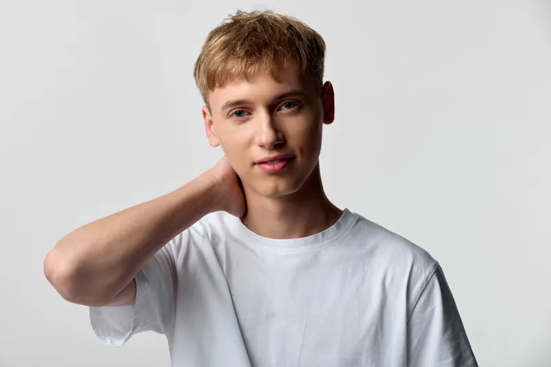 young man, casual clothing, white t shirt, relaxed pose, neutral backdrop, hand on neck, subtle smile, clean versatile look for lifestyle, fashion, stock photography use