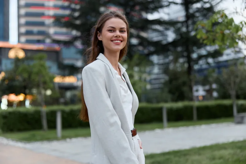 Confident woman in white jacket smiling outdoors urban background business concept professional young adult