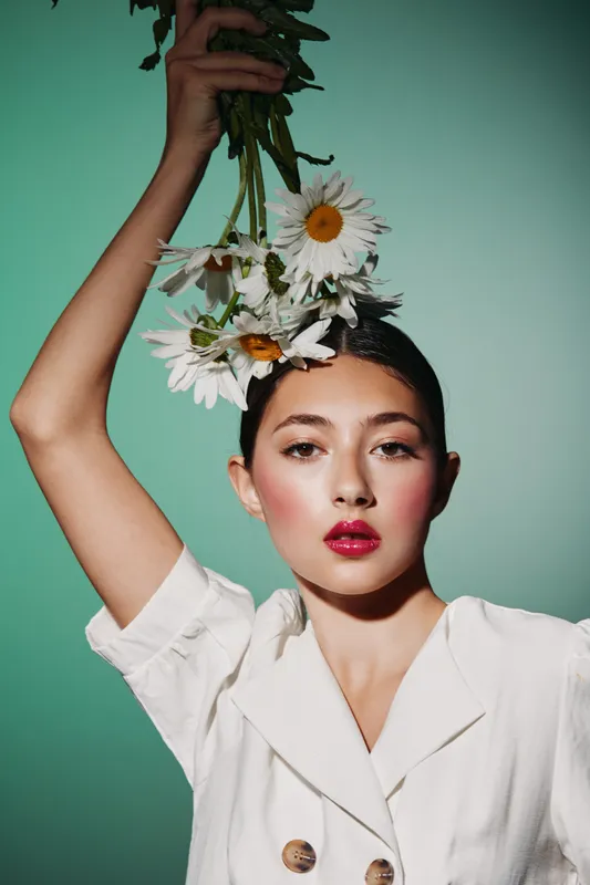 Young woman with fresh makeup holds a bouquet of daisies above her head against a turquoise background. Concept of beauty creative fashion and natural elegance.