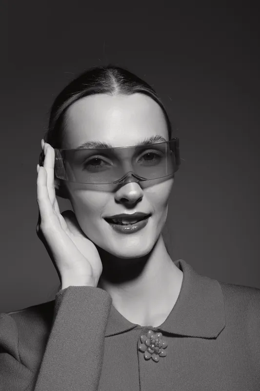 Caucasian woman with fair skin wearing large sunglasses and a textured jacket poses confidently against a dark background. Concept of fashion, style, and elegance.