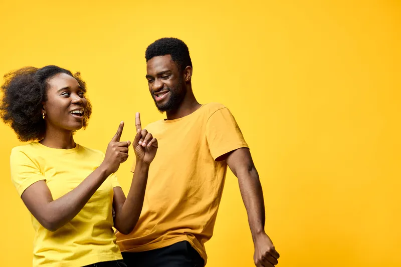 Happy African couple having fun and dancing against a bright yellow background, wearing casual yellow and black clothes, expressing joy and connection